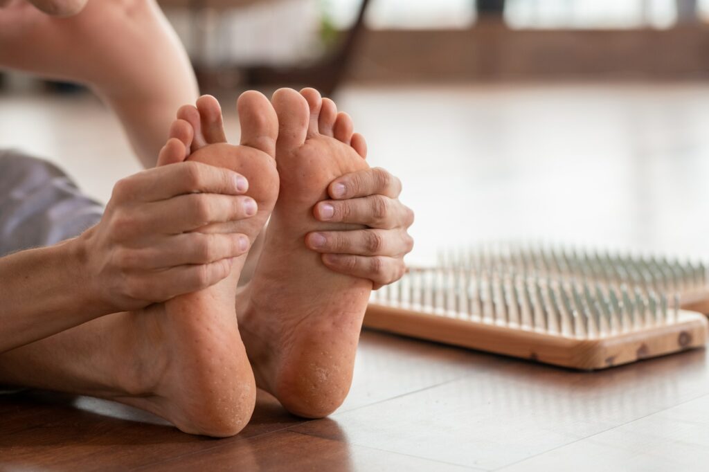 Barefoot man sitting on wooden floor and holding his feet during exercise